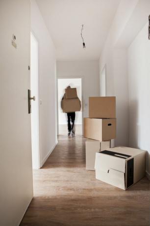 Žmogus iškrauna kartonines dėžes naujo namo prieškambaryje