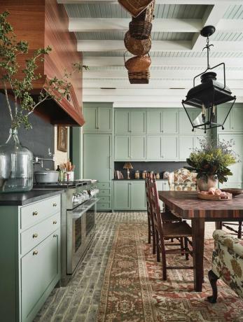 virtuvė, žalios spintos, ploto kilimėlis, medinis valgomojo stalas su medinėmis kėdėmis, medinis gartraukis, žaluma