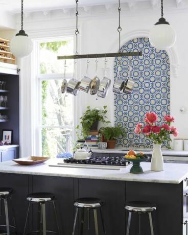 virtuvė, juoda virtuvės sala, nerūdijančio plieno baro kėdės, balto marmuro stalviršiai, juodos kepsninės, mėlynos ir geltonos plytelės