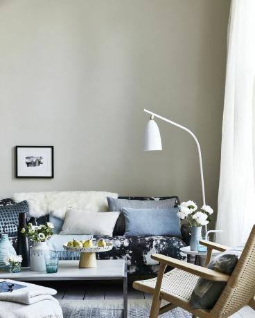neutrali svetainė, svetainė su pagalvėlėmis ant mėlynos spalvos sofos, sulenktas baltas toršeras virš sofos lašeliai, dėmės ir purslų raštai suteikia šiuolaikišką impresionistinę išvaizdą ir atsipalaidavęs